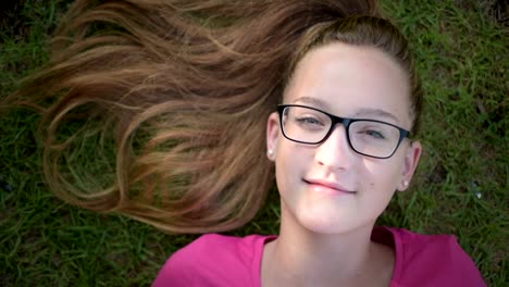 Alegre-teenage-girl-lying-on-the-grass-and-looking-at-the-sky,-realice-la-toma-desde-arriba