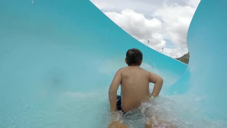 Happy-young-boy-going-down-curved-waterslide-in-slow-motion