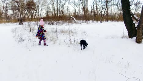 Kleines-Mädchen-spielt-mit-ihren-schwarzen-Labrador-auf-Schnee