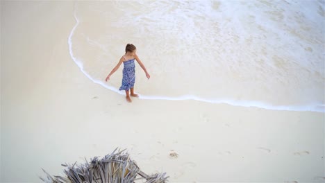 Niña-adorable-con-un-montón-de-diversión-en-aguas-poco-profundas.-Vista-desde-arriba-de-una-playa-desierta-con-agua-de-color-turquesa