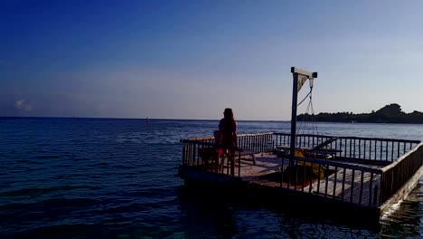 v03832-Aerial-flying-drone-view-of-Maldives-white-sandy-beach-2-people-young-couple-man-woman-relaxing-on-sunny-tropical-paradise-island-with-aqua-blue-sky-sea-water-ocean-4k-floating-pontoon-jetty-sunbathing-together