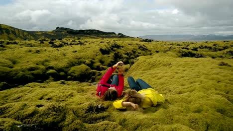Aerial-view-of-the-two-woman-lying-on-the-soft-lava-field-in-Iceland.-Tourists-taking-selfie-on-the-smartphone