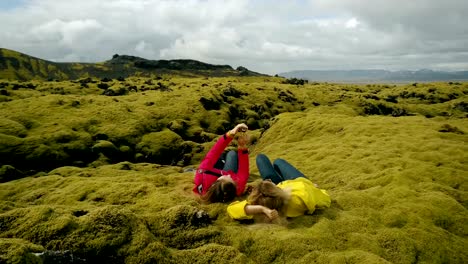 Vista-aérea-de-las-dos-mujeres-en-el-campo-de-lava-suave-en-Islandia.-Turistas-toman-selfie-en-el-smartphone