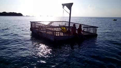 v03838-vuelo-drone-vista-aérea-de-Maldivas-playa-2-personas-pareja-hombre-mujer-relajante-en-la-isla-de-paraíso-tropical-soleado-con-cielo-azul-aqua-agua-mar-4k-flotante-pontoon-embarcadero-el-sol-juntos