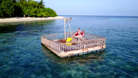 v03840-fliegenden-Drohne-Luftaufnahme-der-Malediven-weißen-Sandstrand-2-Personen-junges-Paar-Mann-Frau-entspannend-auf-sonnigen-tropischen-Inselparadies-mit-Aqua-blau-Himmel-Meer-Wasser-Ozean-4k-schwimmenden-Ponton-Steg-Sonnenbaden-zusammen