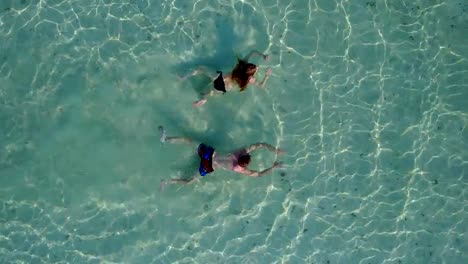 v04199-Aerial-flying-drone-view-of-Maldives-white-sandy-beach-2-people-young-couple-man-woman-swimming-splashing-underwater-on-sunny-tropical-paradise-island-with-aqua-blue-sky-sea-water-ocean-4k