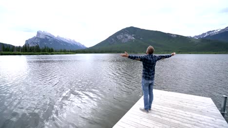 Hombre-joven-de-brazos-extendidos-en-el-muelle-del-lago,-Canadá