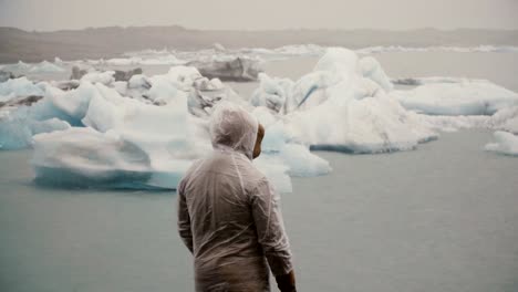 Vista-posterior-de-joven-en-pie-impermeable-en-la-laguna-de-hielo-en-Islandia.-Explorando-la-famosa-vista-solo-de-turista