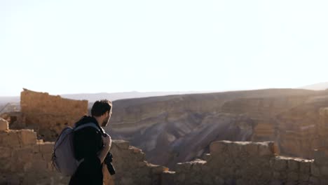 Fotógrafo-profesional-explora-ruinas-antiguas.-Hombre-europeo-con-cámara-y-mochila-cerca-de-vista-a-la-montaña.-Israel-4K