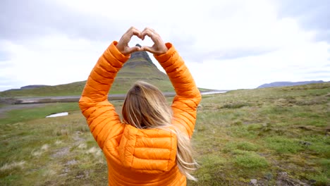 Junge-Frau-in-Island-machen-Herz-Formrahmen-Finger-am-berühmten-Berg-Kirkjufell