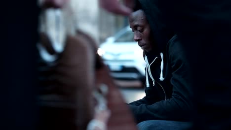 pensive-young-american-african-man-using-smartphone-sitting-in-the-street