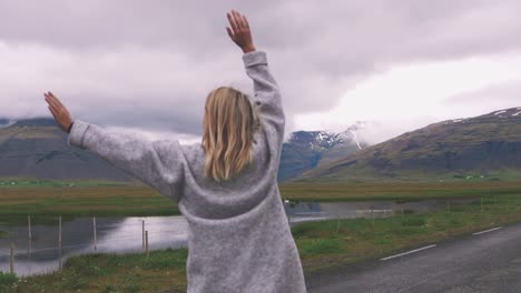 Glückliche-junge-Frau-zu-Fuß-auf-Asphaltstraße-in-Island-und-etwas-Spaß-Aussicht-genießen.-Zeitlupe,-filmische-Schuss