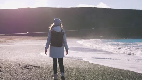 Tourist-woman-with-leather-bagpack-walking-near-the-coastal-landscape-in-Iceland,-slow-motion,-cinematic-shot