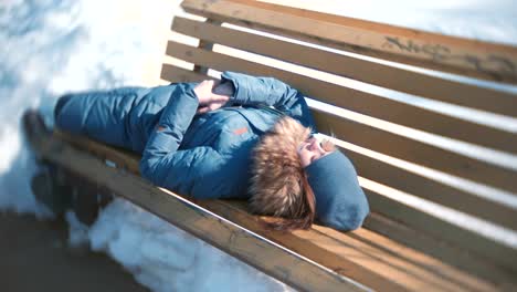 Mujer-joven-durmiendo-en-el-parque-en-un-banco-en-el-invierno.