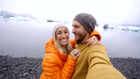 4-K-Video-der-jungen-Paare,-die-Spaß-unter-Selfie-durch-den-Gletschersee-Jökulsárlón-Lagune-in-Island.-Zwei-Personen-Reisen-Liebe-Romantik-Kommunikationskonzept-miteinander-teilen.-Frühling,-Kälte