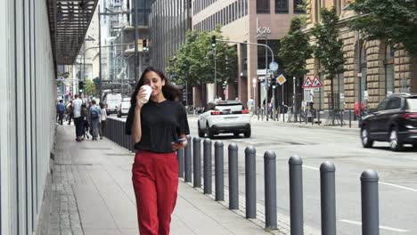 Young-Woman-Walking-on-Sidewalk-Drinking-Coffee-From-a-Paper-Cup