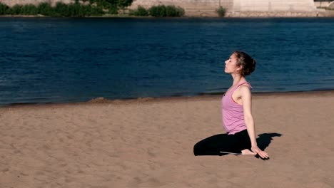 Woman-stretching-yoga-on-the-beach-by-the-river-in-the-city.-Beautiful-city-view.-Breathing-exercise.