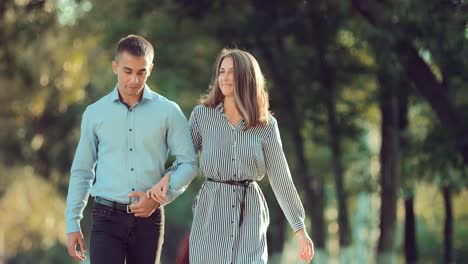 Young-couple-walking-along-the-city-park-together,-go-to-the-camera