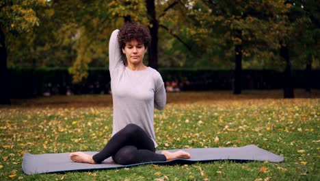 Ernste-junge-Frau-Yogini-ist-Training-im-Park-sitzen-in-Kuh-Gesicht-Pose-mit-Arme-hinter-dem-Rücken-während-der-Open-Air-Praxis-im-Stadtpark.-Natur-und-Gesundheit-Konzept.