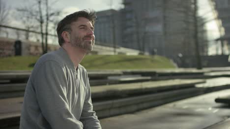 Smiling-middle-aged-man-is-siiting-on-a-bench-in-modern-urban-city-in-autumn