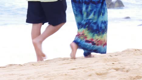 An-older-couple-holding-hands-and-walking-down-the-beach,-starting-close-up-on-their-feet