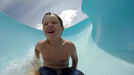 Happy-young-boy-going-down-curved-waterslide-in-slow-motion