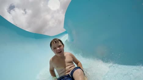 Happy-young-boy-going-down-curved-waterslide-in-slow-motion