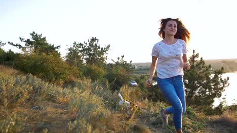 Young-attractive-woman-playing-with-a-dog-Jack-Russell-in-the-meadow-at-sunset-with-sea-background.-slow-motion