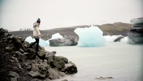 Young-attractive-woman-in-lopapeysa-standing-in-ice-lagoon.-Tourist-exploring-the-famous-sight-of-Iceland-alone