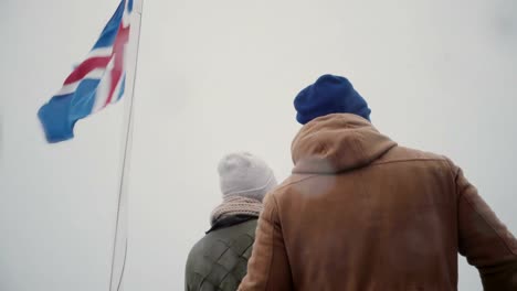 Back-view-of-young-couple-traveling-on-the-ship-with-Icelandic-flag-together.-Man-and-woman-look-on-sea-together