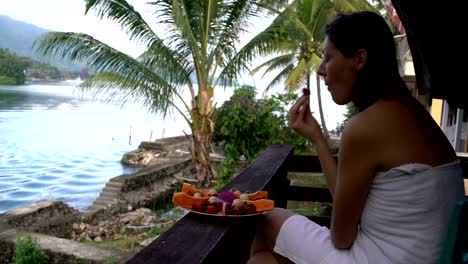 Mujer-comiendo-fresas-sentado-en-una-toalla-contra-el-telón-de-fondo-de-un-lago-y-montañas