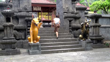 Eine-Frau-in-einem-langen-Rock-steigt-auf-einen-buddhistischen-Tempel-auf-eine-Steintreppe-mit-Statuen