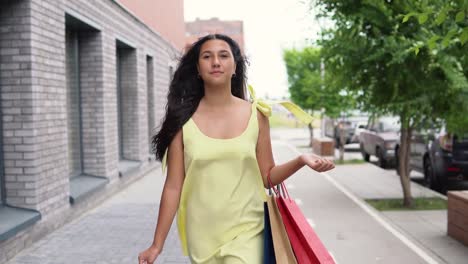 Chica-joven-en-un-vestido-largo-va-alrededor-de-la-ciudad-después-de-comprar-con-buen-humor.-4K