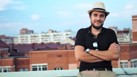 Portrait-of-happy-Caucasian-man-in-hat-with-arms-crossed-outdoor-on-roof-or-balcony