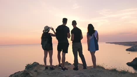 Gruppe-von-jungen-Wanderer-Freunden-reden,-erstaunliche-Meer-und-schönen-Sonnenuntergang-stehen-am-Felsen