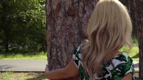 Attractive-woman-touching-bark-of-pine-tree-with-hand-and-walking-around