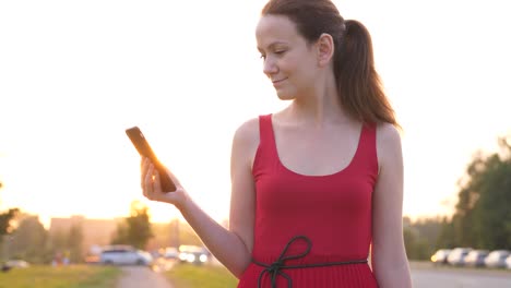 Woman-with-smartphone-standing-on-street-against-road-with-driving-cars