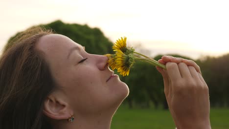 Woman-smells-dandelions-at-sunset,-face-close-up