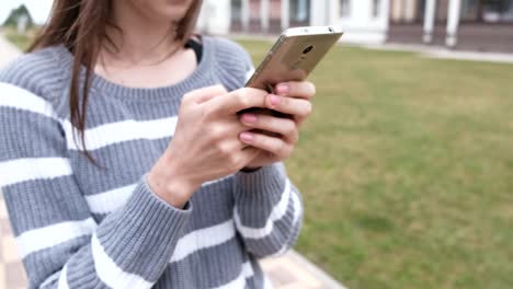 Unrecognizable-brunette-woman-is-reading-something-on-mobile-phone-walking-near-the-home.