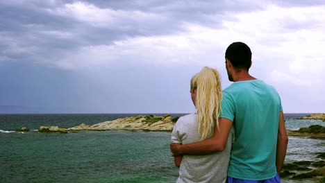 Pareja,-abrazar,-mirar-el-mar-tempestuoso,-Grecia