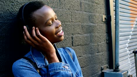 Woman-listening-music-on-headphones-while-leaning-against-wall-4k