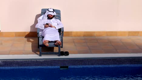 saudi-arabischer-Mann-mit-seinem-Handy-am-Swimmingpool