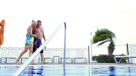 Una-Pareja-de-ancianos-sosteniendo-las-manos-y-caminar-junto-a-la-piscina-del-complejo-turístico