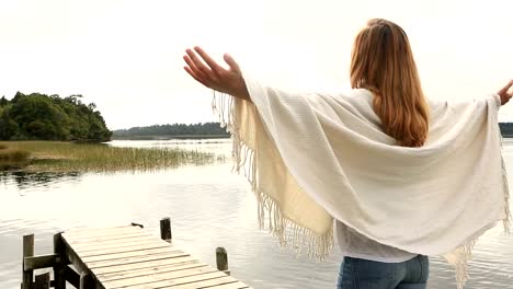 Young-woman-relaxes-on-lake-pier,-stands-arms-outstretched