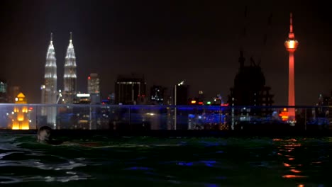 Woman-relaxing-in-rooftop-swimming-pool-at-night,-Kuala-Lumpur