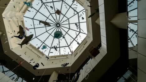PAN-shot-of-glass-ceiling-of-the-shopping-center-with-paper-garlands-on-a-background-of-time-lapse-light-of-the-sun-rays-on-a-blue-sky
