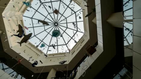 Schwenk-in-der-Glasdecke-des-Shopping-Centers-mit-Papier-Girlanden-auf-einem-Hintergrund-von-Time-Lapse-Licht-der-Sonnenstrahlen-auf-einen-blauen-Himmel