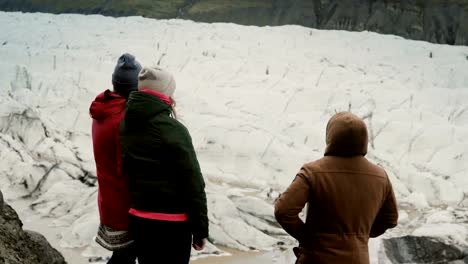 Grupo-de-jóvenes-de-pie-en-la-montaña-y-mostrando-algo,-caminar-en-la-laguna-de-hielo-Vatnajokull-en-Islandia