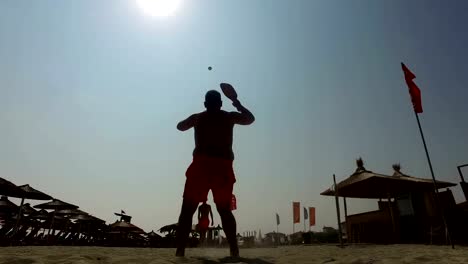 Silueta-de-dos-hombres-jugando-al-tenis-playa-en-la-playa