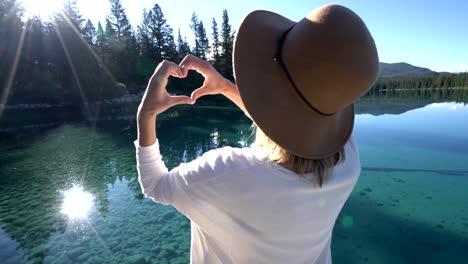 Mujer-joven-en-muelle-de-madera-hace-forma-marco-de-corazón-en-la-naturaleza